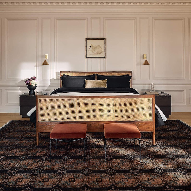 Bedroom with a wooden bed frame, black bedding, and two orange stools on a patterned rug.
