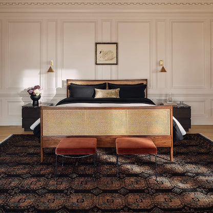 Bedroom with a wooden bed frame, black bedding, and two orange stools on a patterned rug.