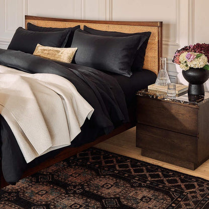 Bedroom with black bedding, wooden headboard, and nightstand with decorative items and Hand knotted Oushak Rug.